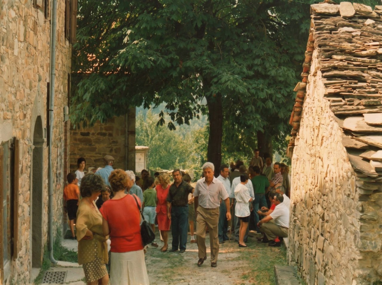 Dipinto: paesani radunati nel vicolo in pietra durante la festa, anni Ottanta